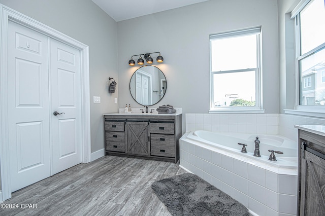 bathroom with hardwood / wood-style flooring, tiled bath, and vanity