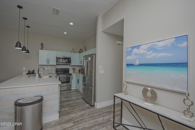 112 Riviera Dr, Panama City Beach, FL 32413 - kitchen with appliances with stainless steel finishes, a sink, a peninsula, light wood-type flooring, and pendant lighting