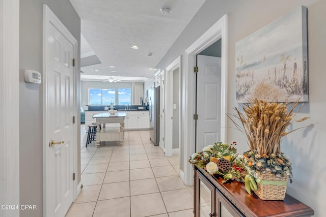 corridor with light tile patterned floors, recessed lighting, baseboards, and a sink