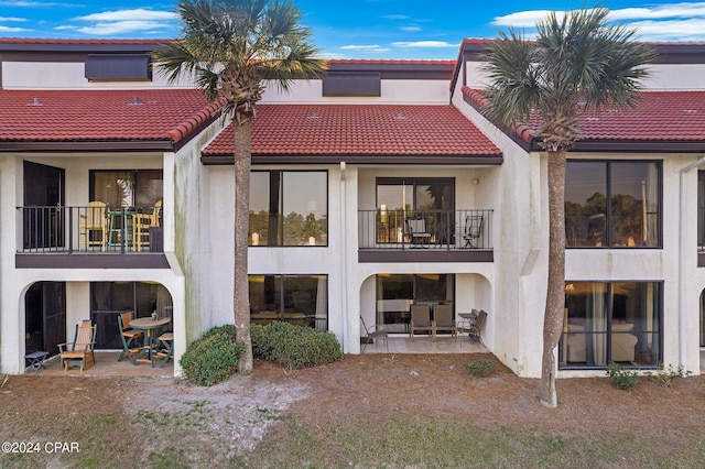 rear view of house with a tile roof, a balcony, a patio area, and stucco siding