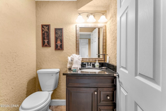 bathroom featuring toilet, a textured wall, and vanity