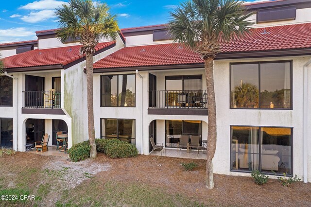 rear view of property with stucco siding, a balcony, a patio, and a tiled roof