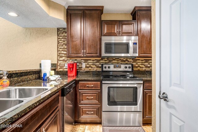 kitchen featuring a textured ceiling, tasteful backsplash, stainless steel appliances, sink, and dark stone counters