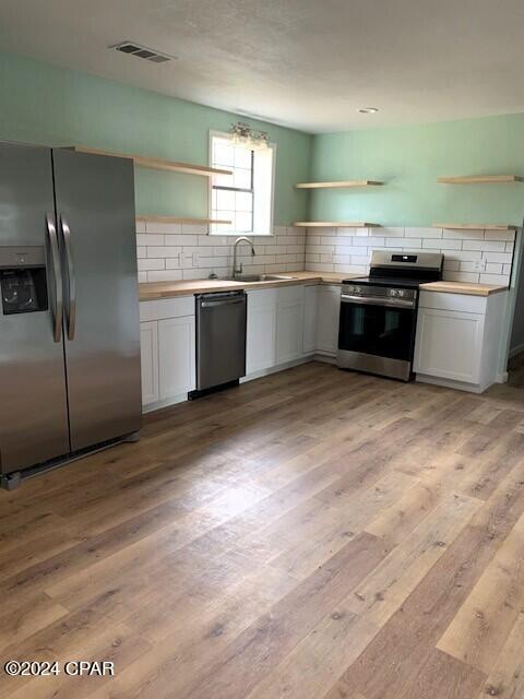 kitchen with white cabinets, stainless steel appliances, backsplash, and light hardwood / wood-style floors