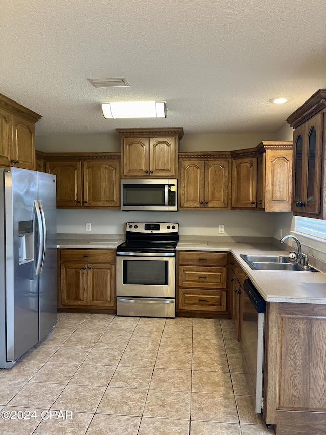 kitchen with a textured ceiling, light tile patterned floors, sink, and appliances with stainless steel finishes