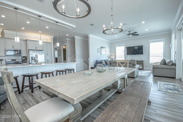 dining area with ceiling fan with notable chandelier, ornamental molding, and hardwood / wood-style floors