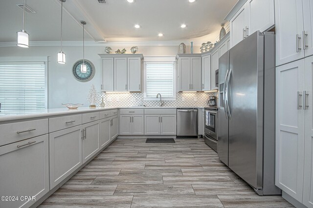 kitchen with appliances with stainless steel finishes, hanging light fixtures, white cabinets, crown molding, and sink