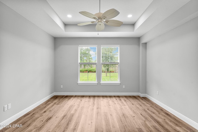 empty room with ceiling fan, a tray ceiling, and light hardwood / wood-style floors