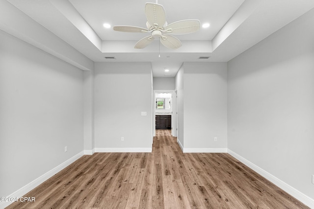 unfurnished room with light hardwood / wood-style flooring, ceiling fan, and a raised ceiling