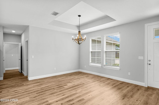 spare room with an inviting chandelier, a tray ceiling, and light hardwood / wood-style floors