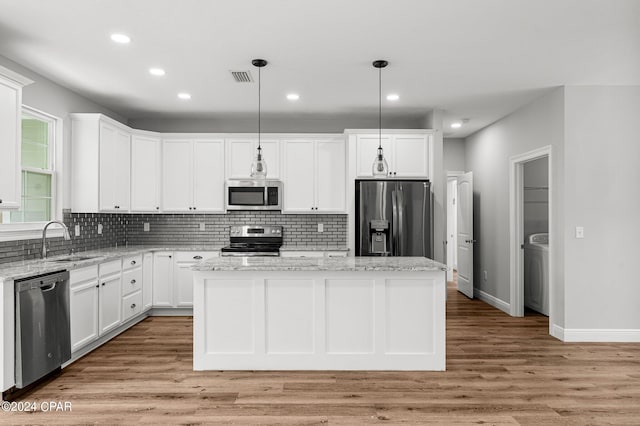 kitchen with appliances with stainless steel finishes, hanging light fixtures, a center island, and light hardwood / wood-style flooring