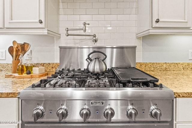 details featuring stainless steel stove, light stone countertops, white cabinets, and tasteful backsplash