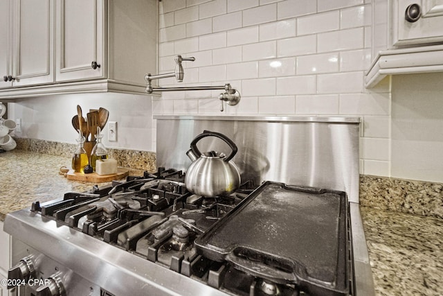 details featuring light stone countertops, stainless steel stove, and tasteful backsplash