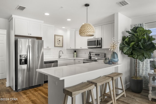 kitchen featuring white cabinetry, hanging light fixtures, stainless steel appliances, dark hardwood / wood-style floors, and kitchen peninsula