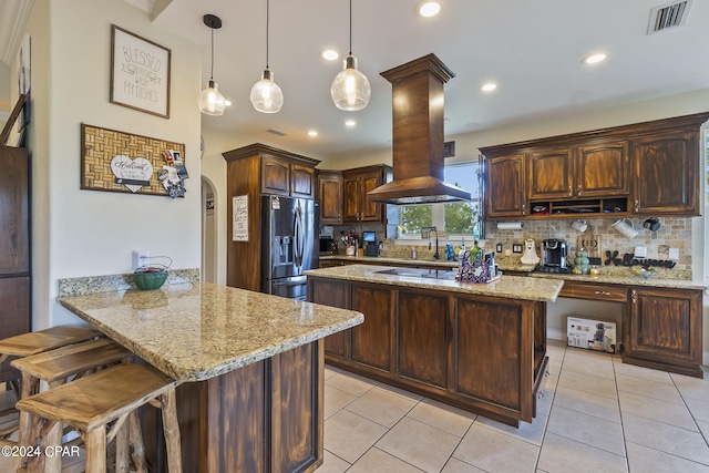 kitchen with kitchen peninsula, hanging light fixtures, backsplash, dark brown cabinetry, and stainless steel fridge