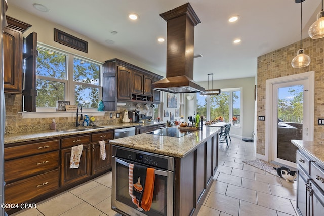 kitchen with sink, island range hood, hanging light fixtures, backsplash, and stainless steel oven