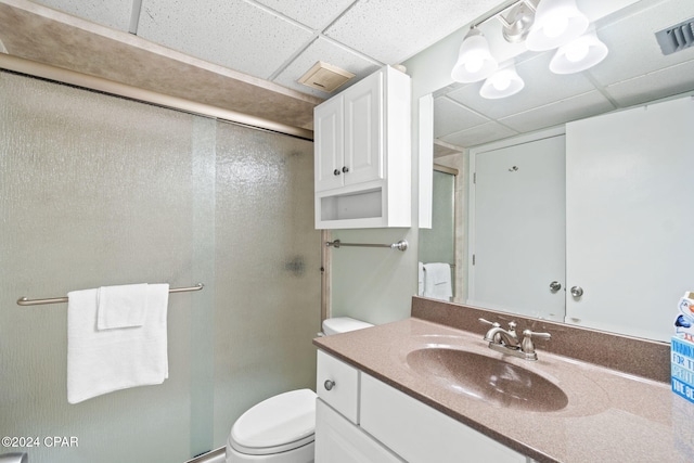 bathroom with toilet, a drop ceiling, vanity, and a shower with door