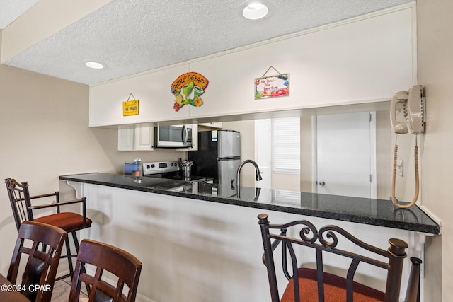 kitchen featuring a kitchen breakfast bar, kitchen peninsula, white cabinetry, appliances with stainless steel finishes, and a textured ceiling