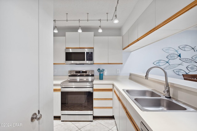 kitchen featuring sink, stainless steel appliances, light tile patterned floors, track lighting, and white cabinets