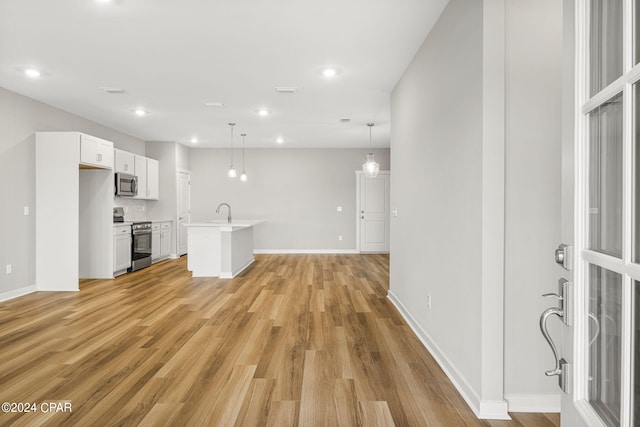 interior space featuring stainless steel appliances, pendant lighting, white cabinets, light hardwood / wood-style flooring, and a center island with sink