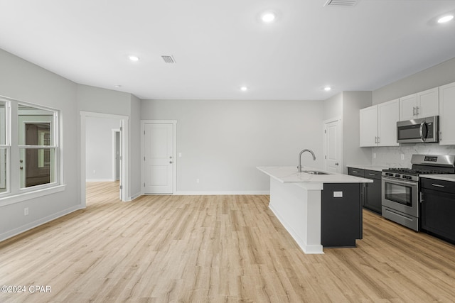 kitchen with white cabinets, an island with sink, light wood-type flooring, sink, and stainless steel appliances