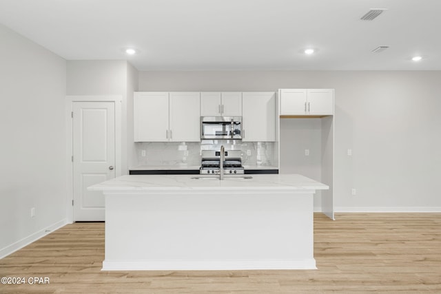 kitchen with stainless steel appliances, a center island with sink, sink, white cabinetry, and light stone counters