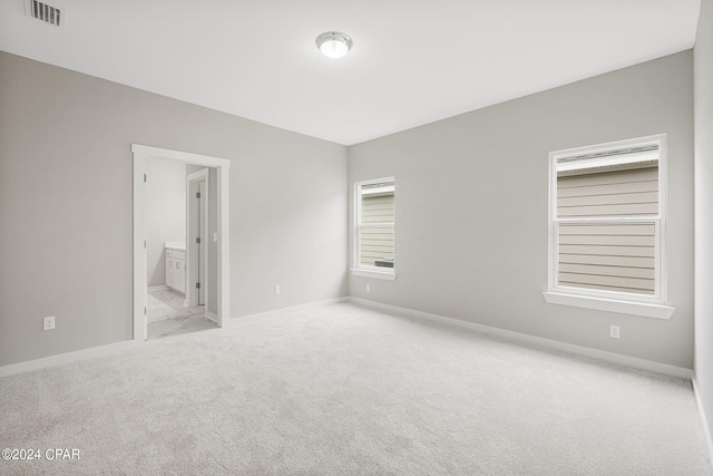 unfurnished bedroom featuring connected bathroom and light carpet