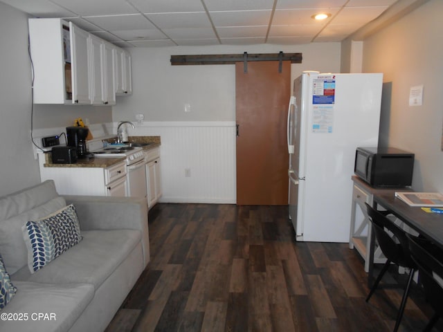 kitchen with white appliances, dark wood-type flooring, white cabinets, a drop ceiling, and a barn door