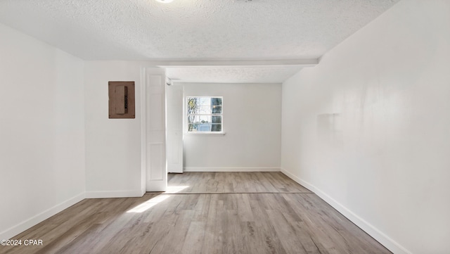 empty room featuring a textured ceiling, light hardwood / wood-style floors, and electric panel