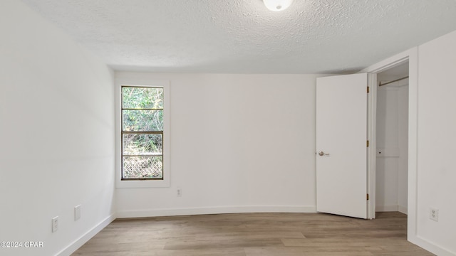 empty room with a textured ceiling and light hardwood / wood-style flooring