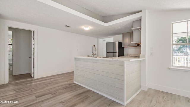 kitchen featuring a textured ceiling, stainless steel fridge, light hardwood / wood-style floors, and kitchen peninsula