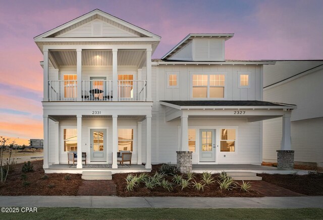 back house at dusk featuring a porch and a balcony