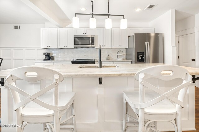 kitchen with appliances with stainless steel finishes, decorative backsplash, and an island with sink