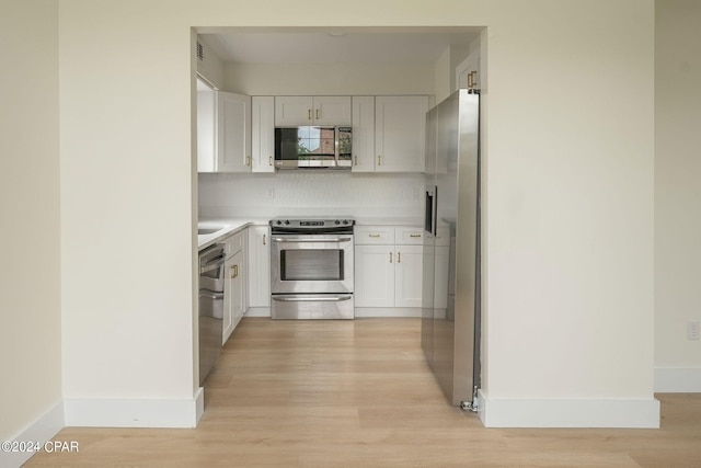 kitchen with stainless steel appliances, white cabinets, light wood-type flooring, and backsplash