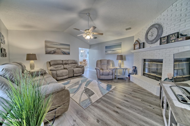 living room with hardwood / wood-style floors, ceiling fan, a textured ceiling, a brick fireplace, and vaulted ceiling