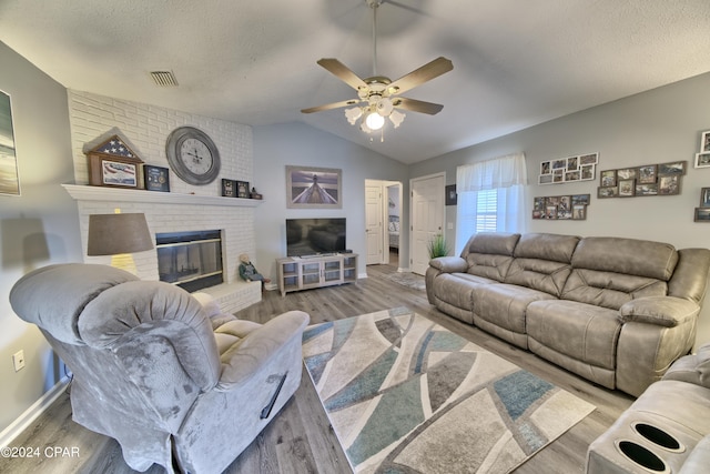 living room featuring light wood-type flooring, a fireplace, a textured ceiling, ceiling fan, and lofted ceiling