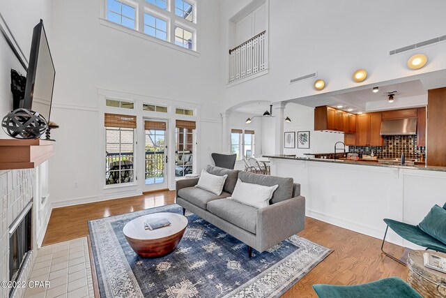 living room with light wood-type flooring, a tiled fireplace, and ornate columns