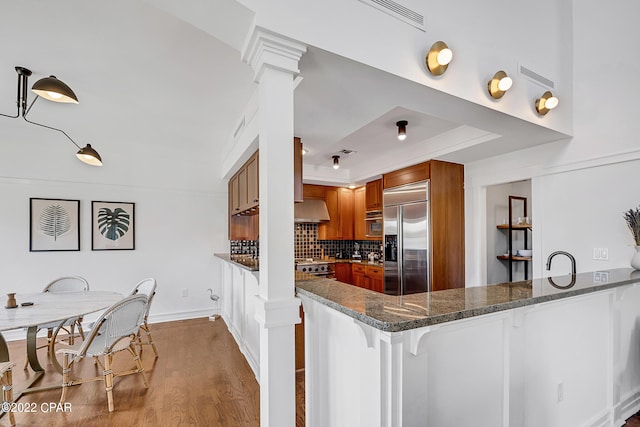 kitchen featuring hardwood / wood-style floors, backsplash, stainless steel appliances, kitchen peninsula, and dark stone counters