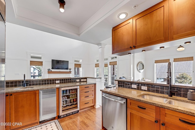 kitchen with beverage cooler, appliances with stainless steel finishes, decorative columns, sink, and light stone counters