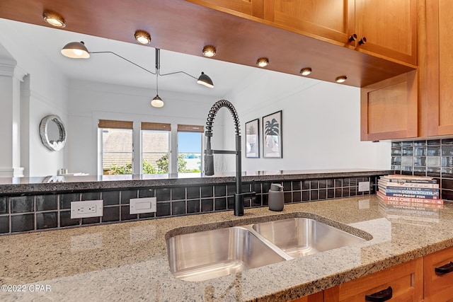 kitchen with decorative light fixtures, light stone countertops, tasteful backsplash, and sink