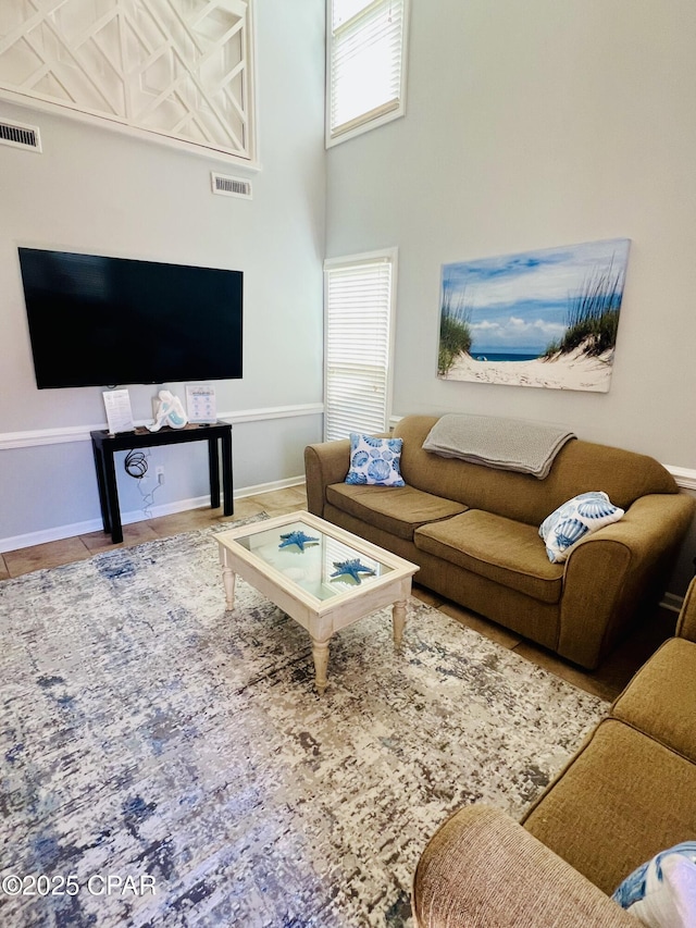 tiled living room with baseboards, a high ceiling, and visible vents