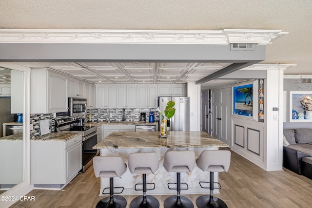 kitchen with light stone countertops, light hardwood / wood-style flooring, appliances with stainless steel finishes, a center island, and white cabinets