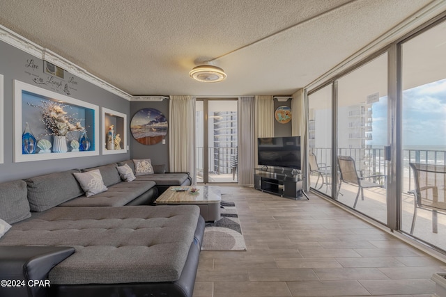 living room featuring a textured ceiling, wood finished floors, visible vents, a wall of windows, and crown molding