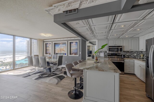 kitchen featuring white cabinets, light wood-type flooring, light stone counters, stainless steel appliances, and a water view