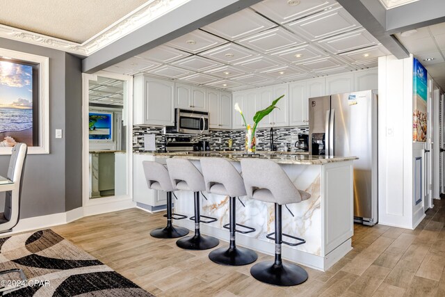 kitchen featuring light stone counters, stainless steel appliances, light hardwood / wood-style floors, white cabinetry, and a breakfast bar