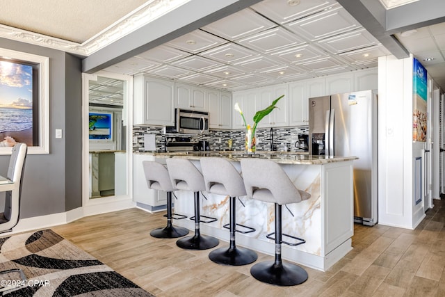 kitchen featuring stainless steel appliances, light stone counters, white cabinets, a breakfast bar, and backsplash