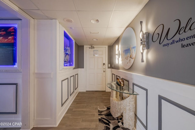 corridor featuring a paneled ceiling, a wainscoted wall, and wood finished floors