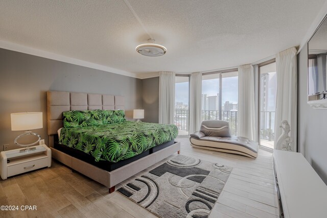 bedroom with a textured ceiling, access to exterior, a wall of windows, and light hardwood / wood-style floors