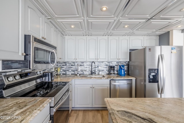 kitchen with stainless steel appliances, light stone countertops, backsplash, sink, and white cabinetry