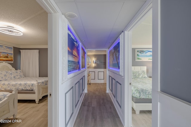 hall featuring a decorative wall, wainscoting, a textured ceiling, wood finished floors, and a drop ceiling